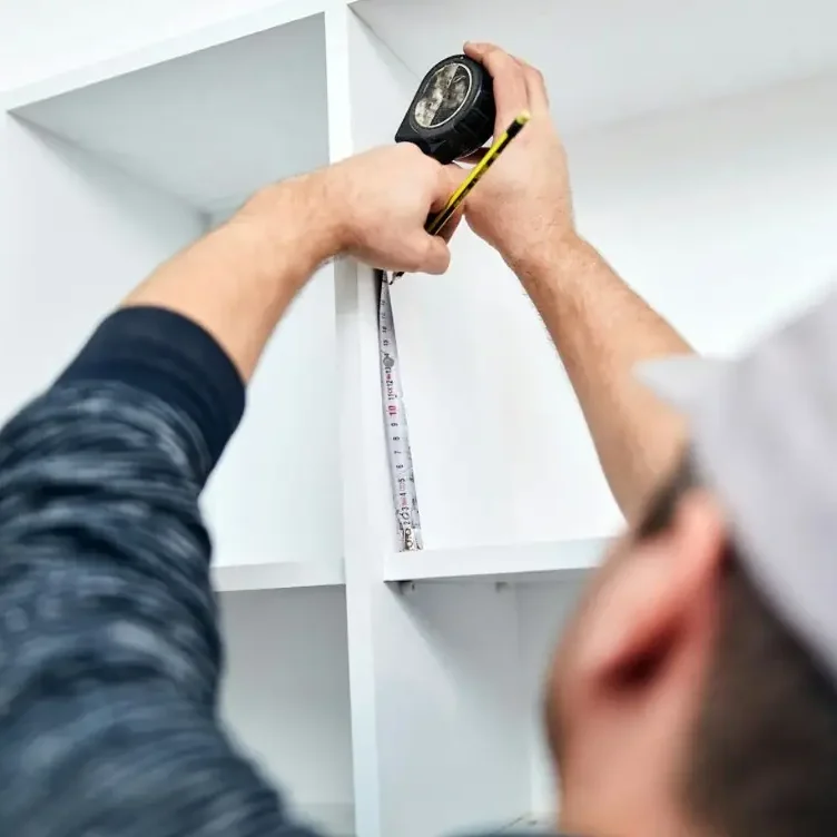 Montage & Reparaturen – Schnelle Hilfe bei kleinen Mängeln Fachgerechte Montage und Kleinreparaturen im Raum Leonberg und Mühlacker – Handwerker misst Möbel mit einem Rollmaßband aus.